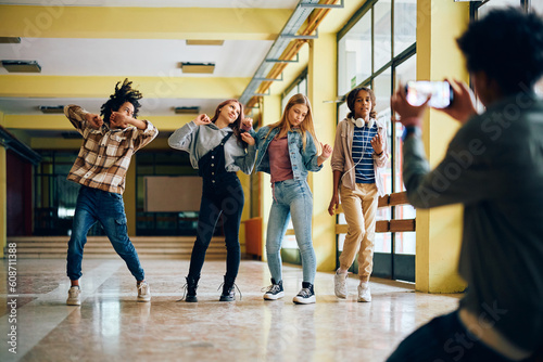 Playful high school students dancing while their friend is taking picture of them with cell phone.
