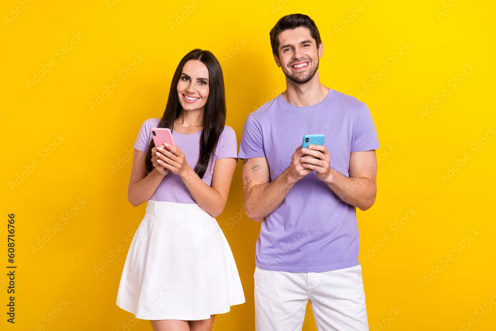 Naklejka premium Portrait of positive partners hold use smart phone chatting eshopping isolated on yellow color background