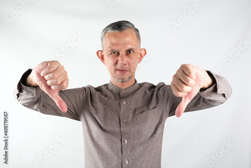 Portrait of Asian Moslem Man looking unhappy showing rejection with thumbs down gesture. Bad expression.
 photo