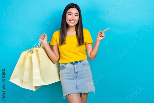 Photo of charming girl hold boutique bags indicate finger empty space promo isolated on blue color background
