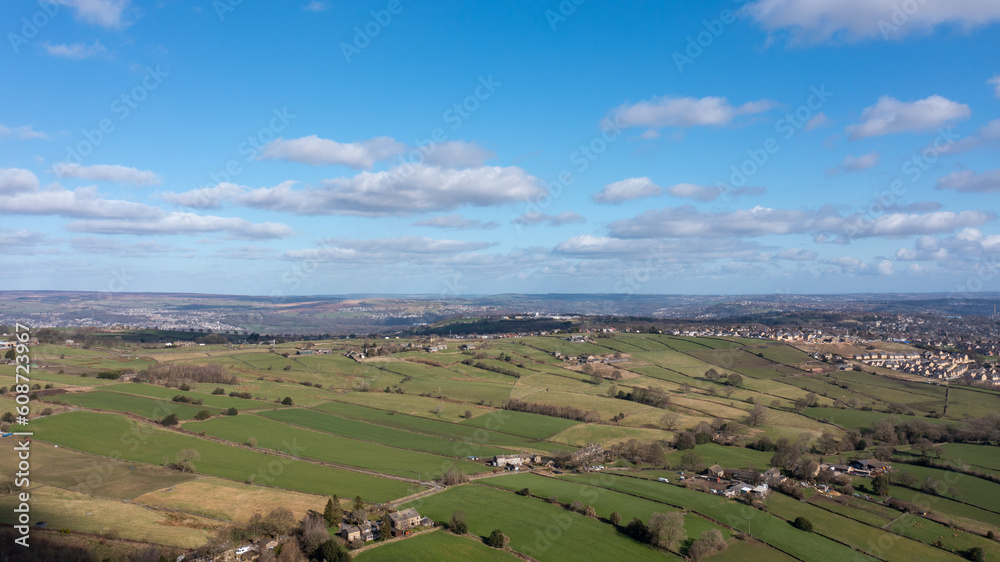 Aerial drone photo of the beautiful town of Thornton in Bradford in the UK showing the farmers fields in the Spring time on a hot sunny day with clouds in the sky.