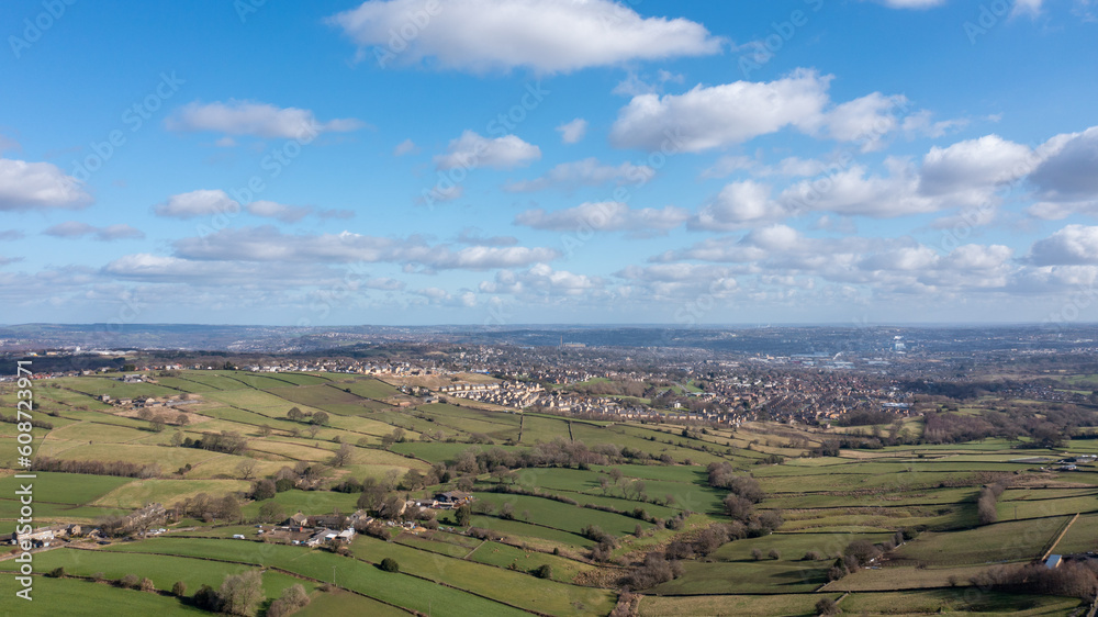 Aerial drone photo of the beautiful town of Thornton in Bradford in the UK showing the farmers fields in the Spring time on a hot sunny day with clouds in the sky.