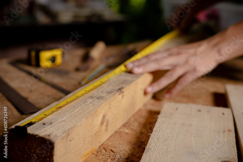 Female use tape measure to assemble wooden pieces. Professional carpenter at work measuring wooden planks.
