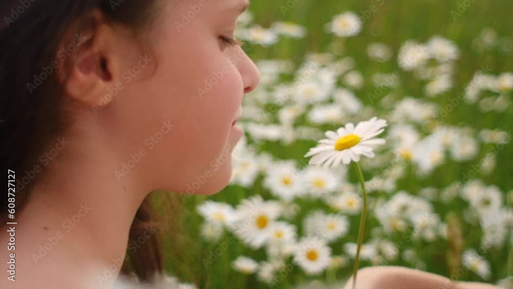 Side view of charming smiling little girl child holding beautiful chamomile flower. Cute happy adorable Caucasian female child sitting in meadow at warm summer day. Childhood concept. Slow motion Side view of charming smiling little girl child holding beautiful chamomile flower. Cute happy adorable Caucasian female child sitting in meadow at warm summer day. Childhood concept. Slow motion