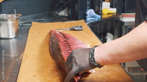 Close-up of the process of cutting tuna fish at the market. Male hands in gloves cutting a large fish with a knife.