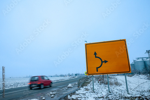 Selective blur on a fast car with a speed blur in winter, with a snowy rural environment, in a european road, with a blank yellow roadsign, in the serbian countryside. photo