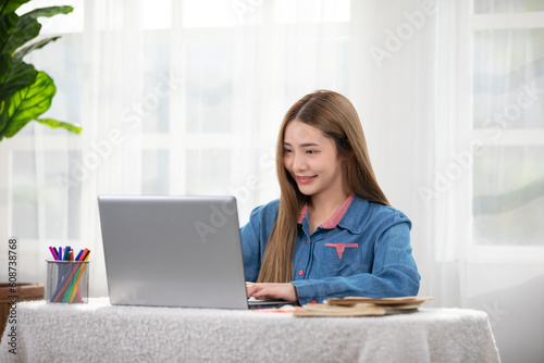 beautiful asian young woman wear casual sit on couch using computer laptop entertain with social media relax smile and laughing.Freelance woman working online sale marketing. Shopping online at home © 220 Selfmade studio