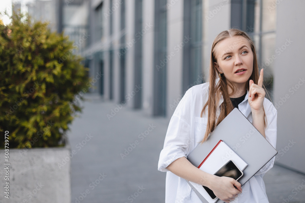 Blonde businesswoman with laptop and book in hand, have idea. point finger up, wow emotions outside office background. Concept of idea and brainstorm. Woman have new ideas or search solutions. Blonde businesswoman with laptop and book in hand, have idea. point finger up, wow emotions outside office background. Concept of idea and brainstorm. Woman have new ideas or search solutions.