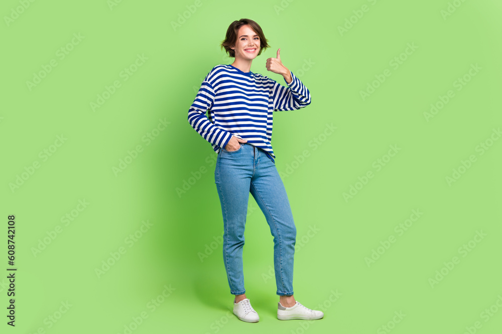 Full length photo of positive nice woman wear sailor shirt showing thumb up good job arm in pocket isolated on green color background Full length photo of positive nice woman wear sailor shirt showing thumb up good job arm in pocket isolated on green color background