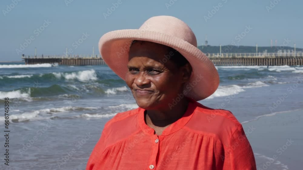 A close-up of an elderly African woman's face as she strolls down the beach in Durban, with waves and a jetty in the distance. A close-up of an elderly African woman's face as she strolls down the beach in Durban, with waves and a jetty in the distance.