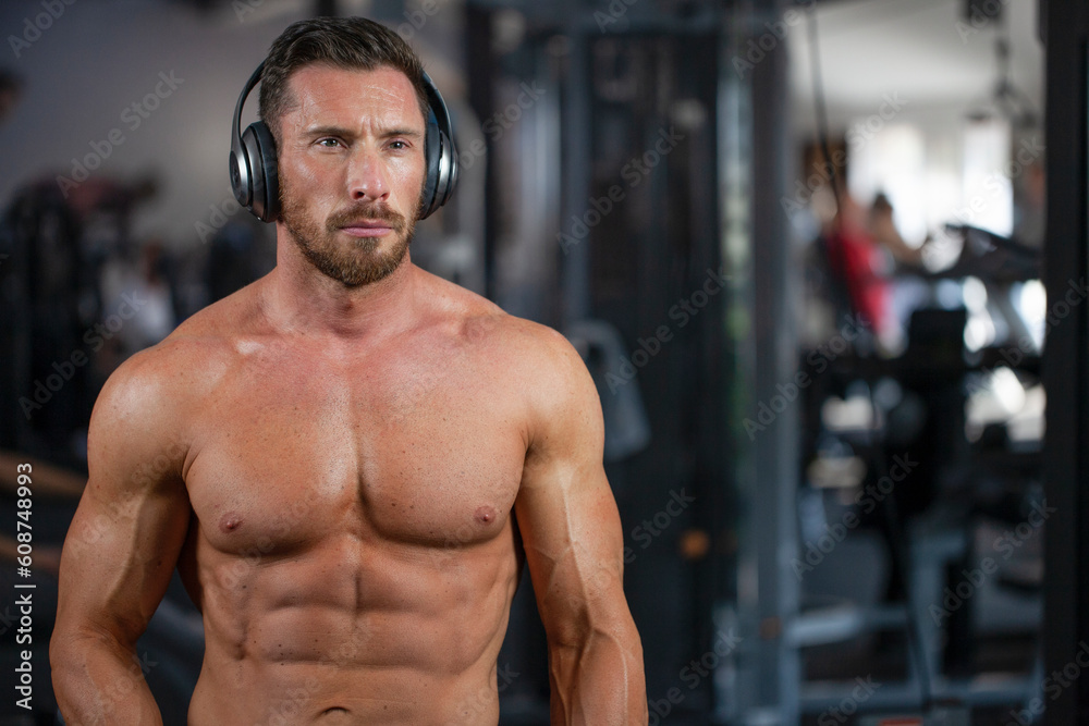Strong sexy muscular bodybuilder guy standing in a gym with headphones. Concept gym, crossfit, bodybuilding. Strong sexy muscular bodybuilder guy standing in a gym with headphones. Concept gym, crossfit, bodybuilding.