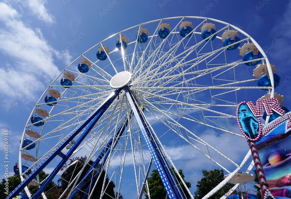 Blau-weißes Riesenrad vor Himmel auf Jahrmarkt bei Sonne am Morgen im Frühling Blau-weißes Riesenrad vor Himmel auf Jahrmarkt bei Sonne am Morgen im Frühling
