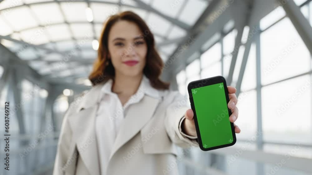 The girl points to the camera a phone with a green screen to replace the image against the background of a geometric pedestrian crossing The girl points to the camera a phone with a green screen to replace the image against the background of a geometric pedestrian crossing