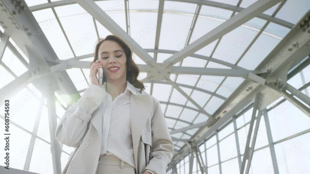A slender young woman in light-colored trousers and a white shirt walks along a crosswalk in bright sunlight, allelically talking on the phone. A slender young woman in light-colored trousers and a white shirt walks along a crosswalk in bright sunlight, allelically talking on the phone.