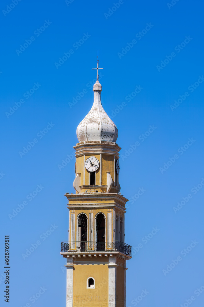 A colorful Christian church bell tower with a clock and a cross against the blue sky on the Ionian Island of Cephalonia Greece. A colorful Christian church bell tower with a clock and a cross against the blue sky on the Ionian Island of Cephalonia Greece.