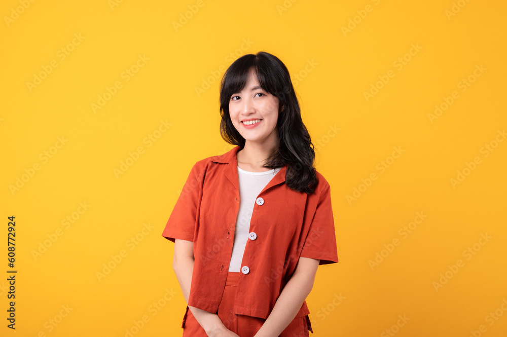 Portrait beautiful young asian woman cute and shy dressed in orange clothes isolated on yellow studio background.