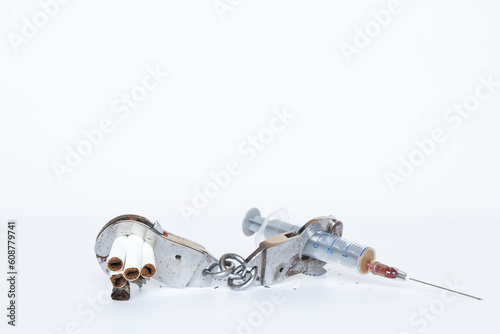 A syringe and cigarettes are handcuffed on a white background, drug addiction