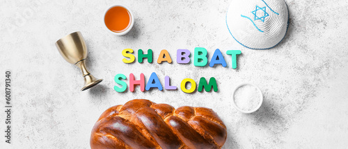 Text SHABBAT SHALOM with traditional challah bread, cup for wine and Jewish cap on grunge background photo