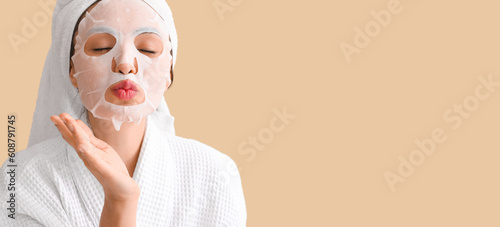 Young woman with applied sheet facial mask blowing kiss on beige background with space for text photo