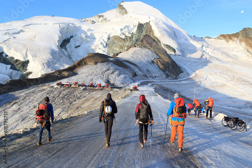 Group of mountaineers with crampons on ski slope ascending towards mountain Allalinhorn and snow mountain panorama in Pennine Alps, Switzerland