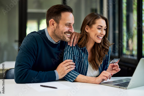 Fotografija A happy woman checking her bank account on a laptop with her male colleague at the workplace