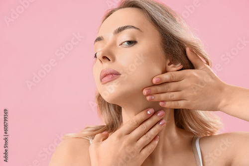 Young woman doing face building exercise on pink background, closeup