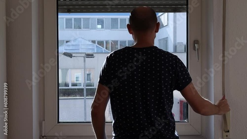 Young man opens the window shutter and looks out the window