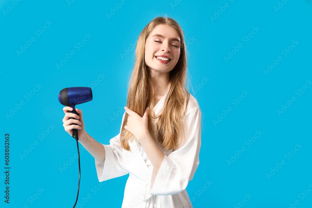 Young blonde woman with hair dryer on blue background Young blonde woman with hair dryer on blue background