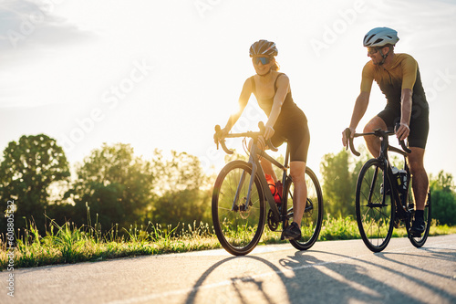 Fototapeta Couple riding bicycles outside of the city and wearing helmets and sunglasses