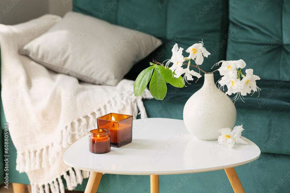 branch of white rhododendron in vase and burning candles  in modern cozy interior