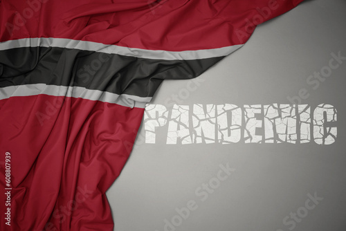waving colorful national flag of trinidad and tobago on a gray background with broken text pandemic. concept. photo