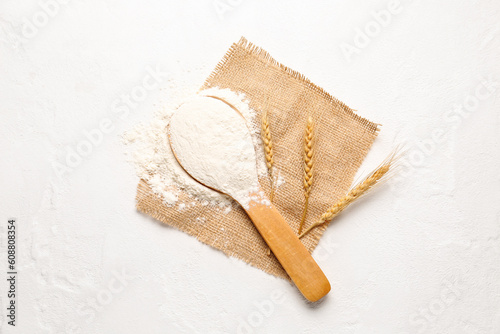 Wooden spoon with flour and wheat ears on white background