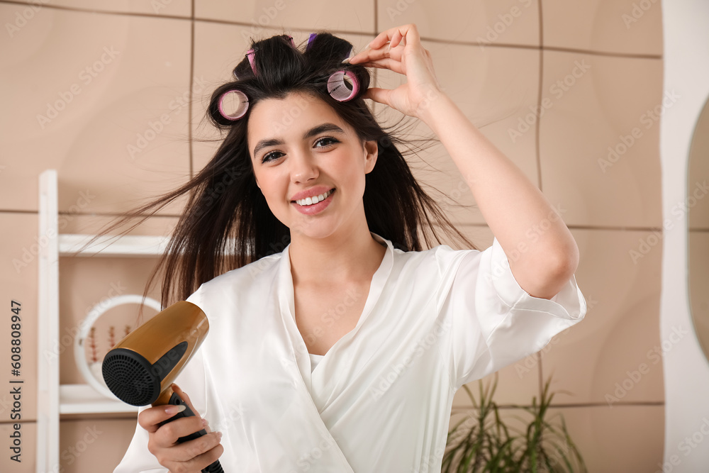 Pretty young woman with hair dryer and curlers in bathroom Stock Photo Adobe Stock