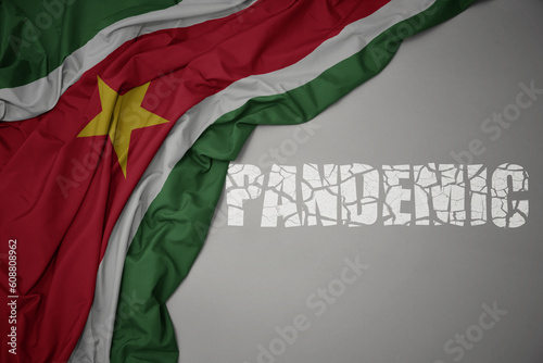 waving colorful national flag of suriname on a gray background with broken text pandemic. concept.