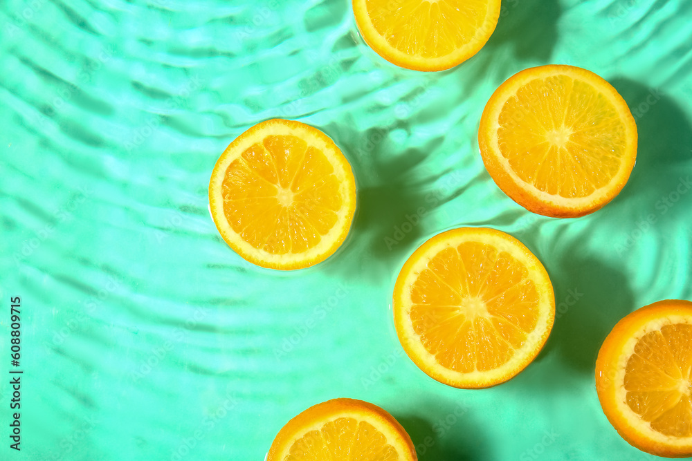 Fototapeta premium Slices of fresh orange in water on turquoise background