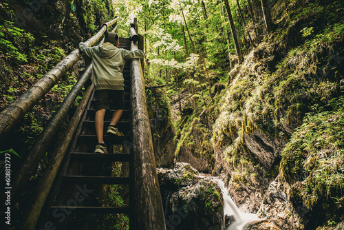 View of boy climbing the steps of a wooden walkway next to white water cascading down the Dr. Vogelgesang-Klamm gorge in Spital am Pyhrn, Austria