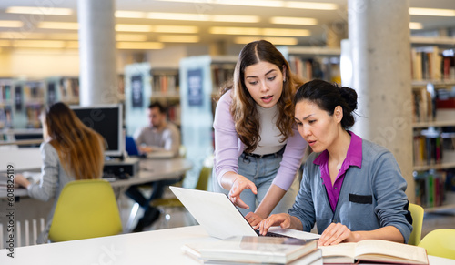 Smiling woman university student offering help colleague preparing to exam at library © JackF