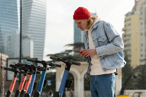 Interested Scandinavian hipster guy explores scooter rental smartphone app for eco-friendly urban mobility. Focused concentrated young european man scans qr code of individual transport in city center