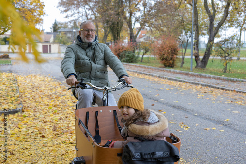 Elderly happy father with a child riding cargo bike in countryside 