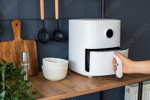 Woman at home using an air fryer. Making healthy food, frying without the use of oil.
