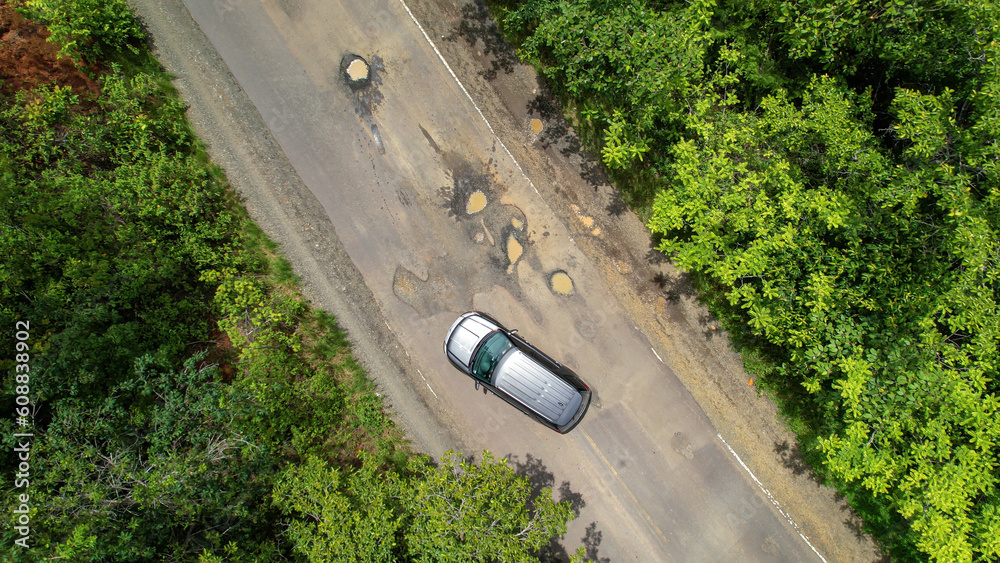AERIAL TOP DOWN: Careful driving of car that tries to avoid dangerous road pits - obrazy, fototapety, plakaty 