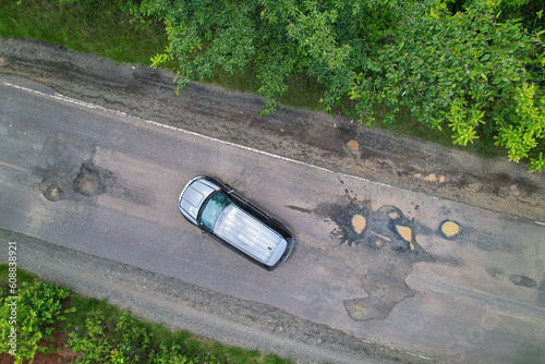 AERIAL TOP DOWN Black car manoeuvres between big and dangerous potholes on road