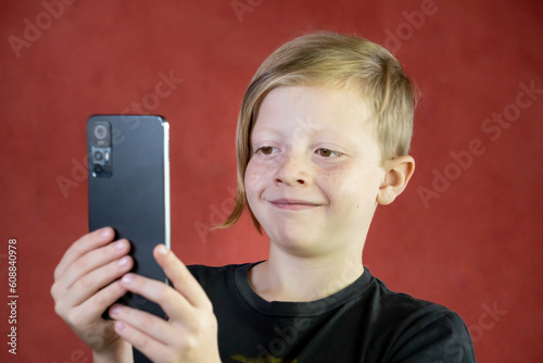 Niño rubio con teléfono movil sonriente con fondo rojo