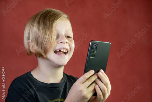 Niño rubio feliz con teléfono movil sonriente con fondo rojo