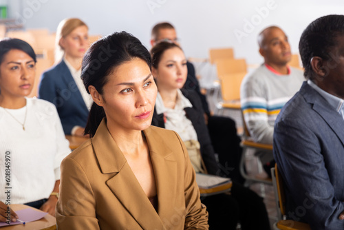 Focused asian businesswoman sitting with colleagues in conference room during corporate seminar