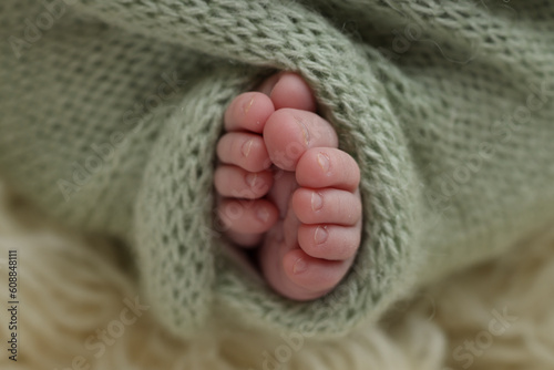 Tiny foot of a newborn. Soft feet of a newborn in a green, pistachio, olive woolen blanket on a white flaccati background. Macro photo of the toes, heels and feet of a newborn.