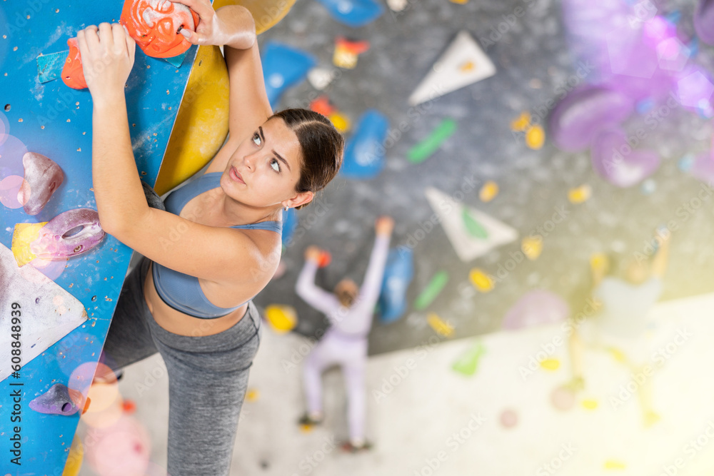 Fototapeta premium Young athletic woman practicing rock climbing on climbing wall..