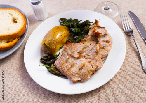 Baked piece of pork with slices of potato and green peppers served in a plate with a glass of wine