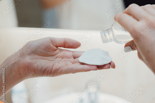 After showering the body and head wrapped in a towel, women's hands apply a moisturizing skin lotion to a cotton pad to wipe the face.