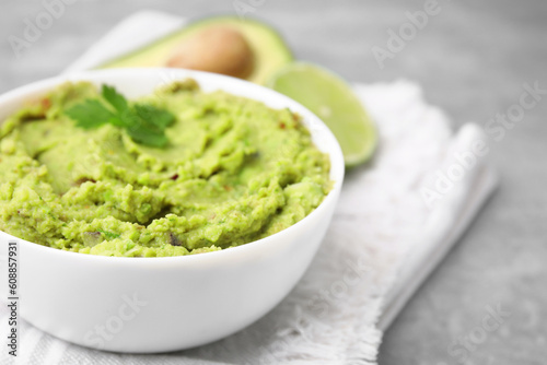 Bowl of delicious guacamole and ingredients on grey table, closeup. Space for text
